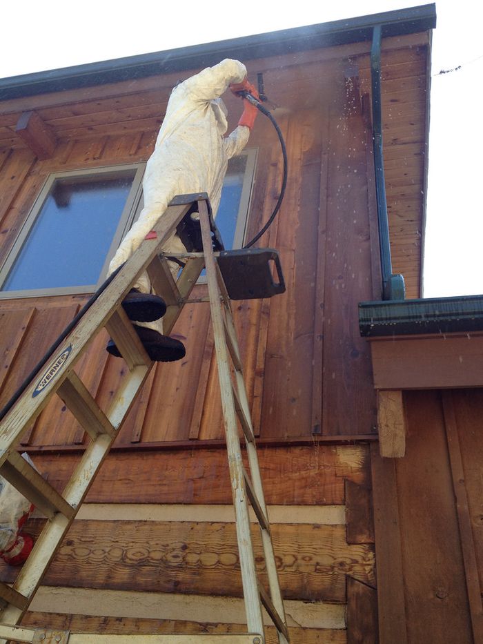 Worker washing a building exterior from a ladder